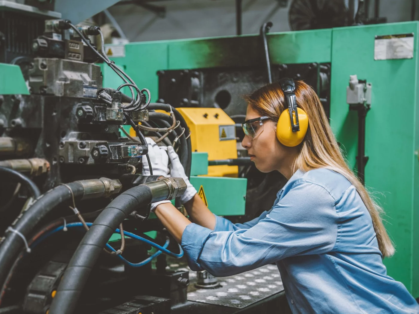 Eine Anlagemechanikerin überprüft eine CNC-Maschine, die Werkstücke mit hoher Präzision automatisch herstellt.