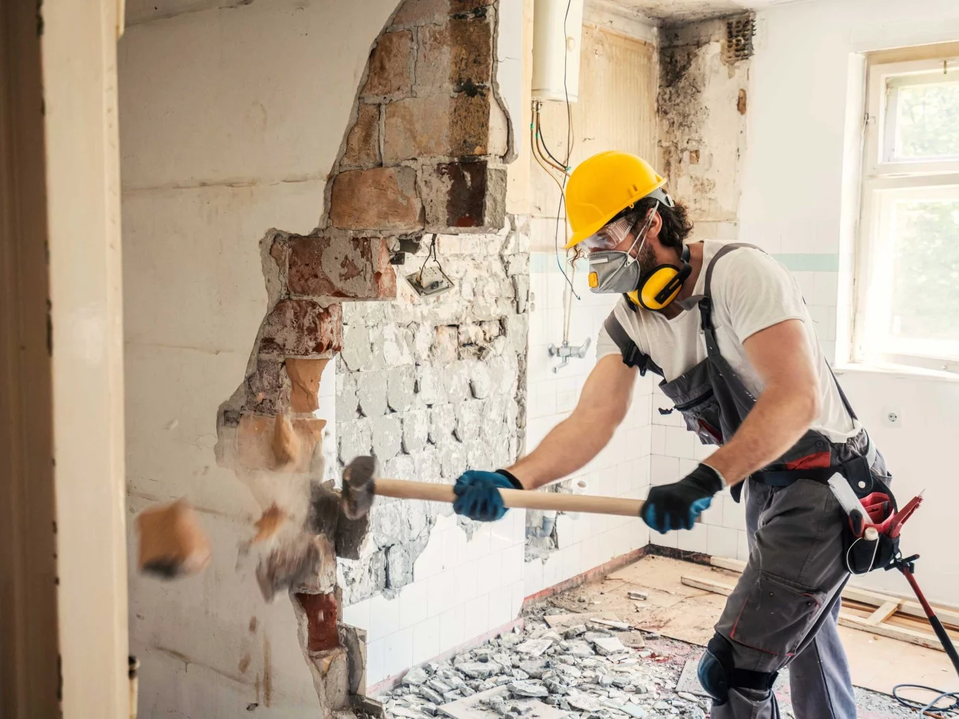 Ein Bauwerksmechaniker für Abbruch und Betontrenntechnik schlägt mit einem Hammer eine Wand in einem Wohngebäude ein.