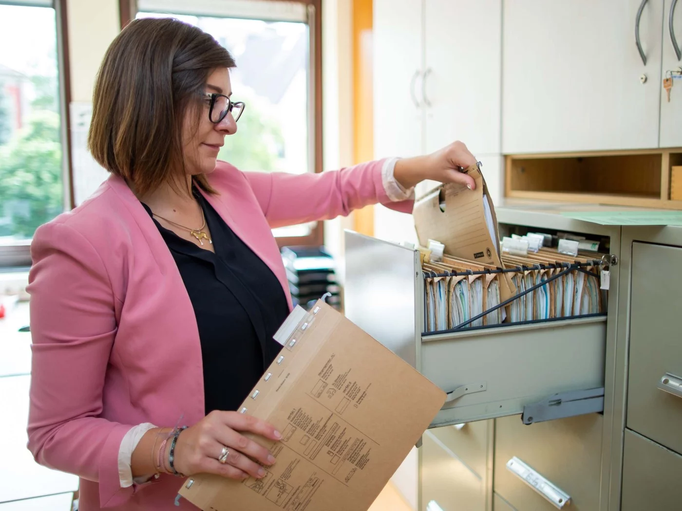Eine Kauffrau für Büromanagement holt sich Akten aus dem Ordner.