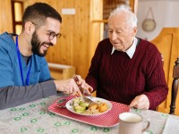 Ein Altenpfleger unterstützt einen Senior beim Mittagsessen.