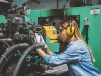 Eine Anlagemechanikerin überprüft eine CNC-Maschine, die Werkstücke mit hoher Präzision automatisch herstellt.