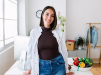 Eine Frau in einem weißen Kittel steht an einem Schreibtisch, auf dem eine Schüssel mit frischem Obst und Gemüse platziert ist.
