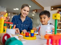 Eine Ergotherapeutin spielt mit zwei Kindern, um die Feinmotorik eines Jungen mit Bausteinen zu fördern.