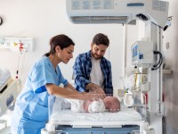 Eine Gesundheits- und Kinderkrankenpflegerin kontrolliert den Gesundheitszustand eines Neugeborenen. 