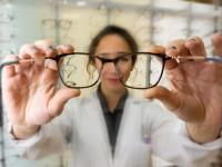Eine Augenoptikerin reicht einem Kunden seine neue Brille zur Anprobe.