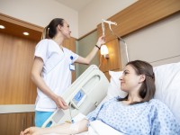Eine Gesundheits- und Krankenpflegerin überprüft die Einstellung des Tropfes einer Patientin, die im Krankenbett liegt.
