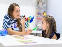 Eine Logopädin und ein Vorschulkind sitzen an einem Tisch und üben spielerisch die korrekte Aussprache von Silben.