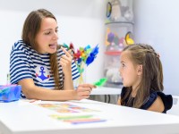 Eine Logopädin und ein Vorschulkind sitzen an einem Tisch und üben spielerisch die korrekte Aussprache von Silben.