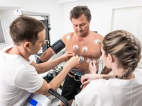 Eine medizinische Technologin und ein Technologe für Funktionsdiagnostik befestigen Messelektroden am Oberkörper eines Patienten. 