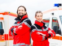 Ein Rettungssanitäterteam in rot-weißen Uniformen steht vor zwei Krankenwägen, bereit für den nächsten Einsatz.