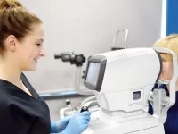 Eine Orthoptistin führt einen Sehtest mit einem medizinischen Gerät bei einem Kind durch.