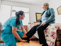 Eine Pflegefachfrau unterstützt während eines Hausbesuchs eine Seniorin beim Anziehen.