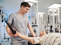 Ein Physiotherapeut einer Rehaeinrichtung unterstützt einen älteren Herrn dabei, seine Mobilität zurückzugewinnen. 