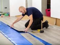 Ein Bodenleger verlegt Vinylboden mit Klickverbindung auf einer Trittschalldämmung.