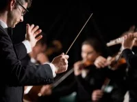 Ein Ensembleleiter hält einen Taktstock, mit dem er ein Orchester anleitet. 