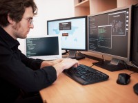 Ein Assistent für technische Informatik sitzt an seinem Schreibtisch und programmiert ein internationales Netzwerk am Computer.