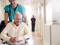 Ein Gesundheits- und Krankenpflegehelfer bringt einen entlassenen Patienten mit dem Rollstuhl zum Ausgang des Krankenhaus.