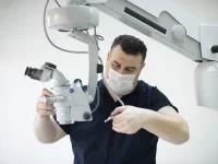 Ein technischer Assistent für medizinische Gerätetechnik wartet ein medizinisches Mikroskop. Dabei trägt er einen Mundschutz.