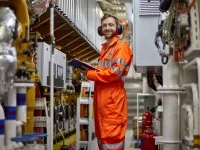 Ein schiffsbetriebstechnischer Assistent steht mit einem Klemmbrett in der Hand im Maschinenraum eines Schiffes.