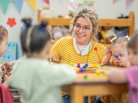 Eine sozialpädagogische Assistentin/ Kinderpflegerin spielt mit einer Kleinkindergruppe in einem Kinderhort.