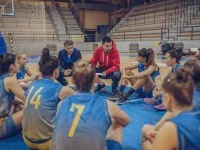 Ein Sportassistent und ein Trainiersitzen mit ihrer Mannschaft auf dem Boden der Sporthalle und besprechen.