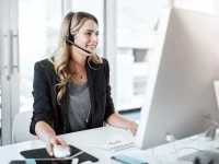 Eine kaufmännische Assistentin / Wirtschaftsassistentin für Informationsverarbeitung führt ein Telefongespräch mit einem Headset, während sie vor ihrem Computer im Büro sitzt.