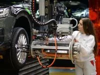 Eine Fertigungsmechanikerin bringt an einem Fließband ein Rad an einem Auto an. 