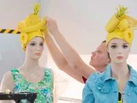 Eine Gestalterin für visuelles Marketing schmückt zwei Schaufensterpuppen mit augefallenen Kopfbedeckungen.