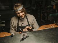Eine Goldschmiedin arbeitet in ihrer Werkstatt an Schmuck.