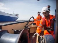 Zwei Hafenschiffer auf einem Schlepper holen ein Seil ein.