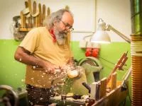 Ein Holzspielzeugmacher drechselt aus einem Holzstück den Kopf einer Spielzeugfigur.