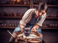 Eine Keramikerin bemalt in ihrem Atelier eine kleine Vase auf der Drehscheibe.