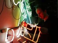 Ein Leuchtröhrenglasbläser prüft eine Neonreklame in der Neonmanufactur in Berlin.