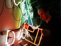 Ein Leuchtröhrenglasbläser prüft eine Neonreklame in der Neonmanufactur in Berlin.