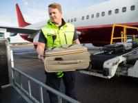 Ein Luftverkehrskaufmann hebt Gepäck von einem Flugzeug auf einen Gepäckwagen.