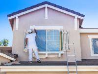Ein Maler und Lackierer bemalt die Fensterläden und -rahmen an einem Haus mit weißer Farbe.