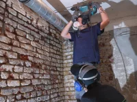 Zwei Holz- und Bautenschützer arbeiten an einer Ziegelwand.