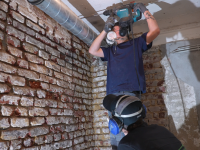 Zwei Holz- und Bautenschützer arbeiten an einer Ziegelwand.