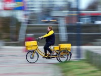 Eine Fachkraft für Kurier-, Express- und Postdienstleistungen der Deutschen Post fährt mit ihrem Dienstfahrrad durch ein Wohngebiet in Schwerin.