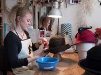 Eine Modistin bügelt eine Hutkrempe in einem Atelier.
