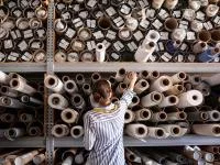 Eine Produktgestalterin - Textil wählt Stoff aus einem Stapel von Rollen in einer Textilwerkstatt aus.