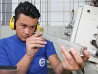 Eine Produktionsfachkraft Chemie der Firma Hermes Schleifmittel kontrolliert ein Werkstück aus Metall.
