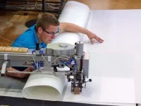 Ein Segelmacher näht mit einer speziellen, im Fußboden eingelassenen Nähmaschine verschiedene Teile eines Segels zusammen.