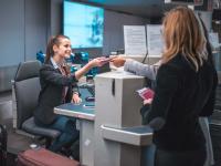 Eine Servicekauffrau im Luftverkehr prüft am Check-in-Schalter die Pässe von zwei Passagieren.