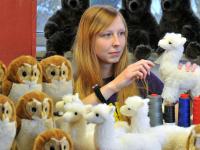 Eine Spielzeugherstellerin kämmt in der Werkstatt die neu hergestellten Alpakas und Eulen aus Plüsch.