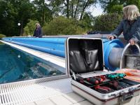 Zwei Technische Konfektionäre installieren die Abdeckplane für das 50-Meter-Becken eines Freibads.