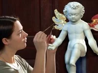 Eine Vergolderin belegt die Flügel einer Engelfigur aus dem 17. Jahrhundert mit 24-karätigem Blattgold. 