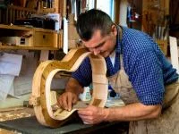 Ein Zupfinstrumentenmacher schleift die Seitenwand eines Gitarrenkorpus.